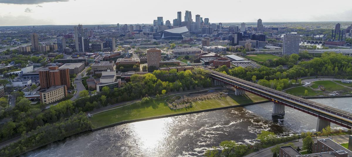 Aerial Photograph of the Mississippi River, the Washington Ave Bridge, and West Bank with Cedar Riverside and downtown Minneapolis in the distance.