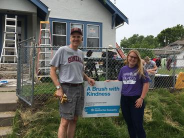 Photograph of Carl Adamek and Shelby Vraspier standing in front of an A Brush with Kindness project where a house is being painted.
