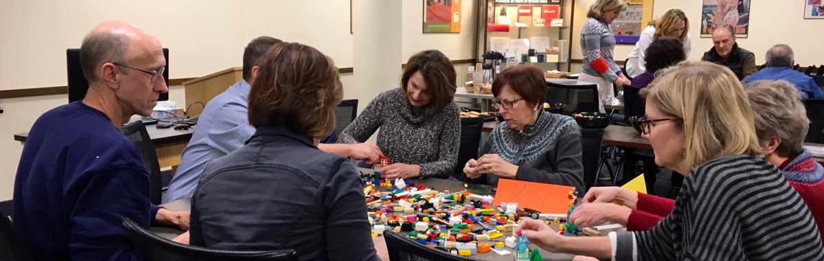 Photograph of a group of people sitting at a table building something out of building blocks.